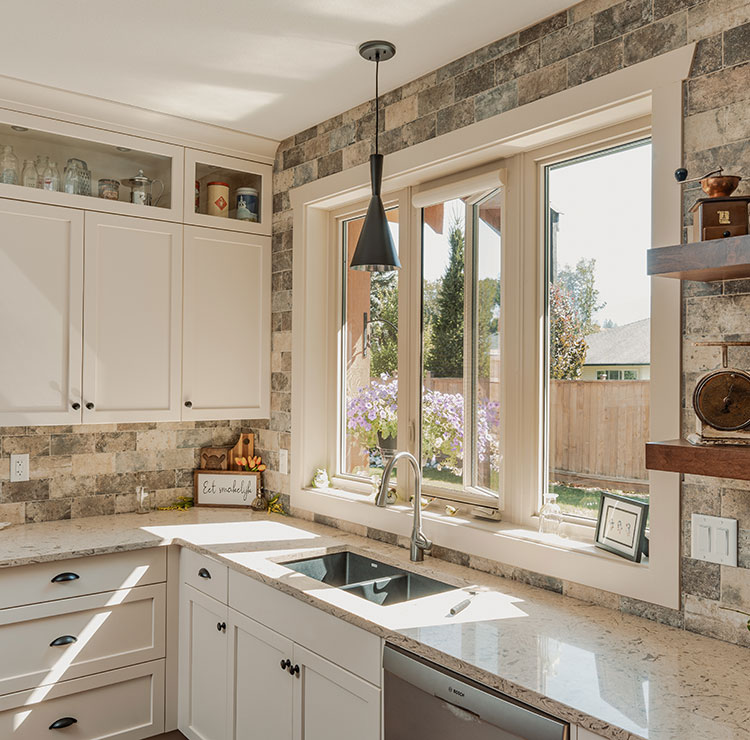Farmhouse kitchen with white cabinets and stone backsplash, featuring bright casement window with rustic decor