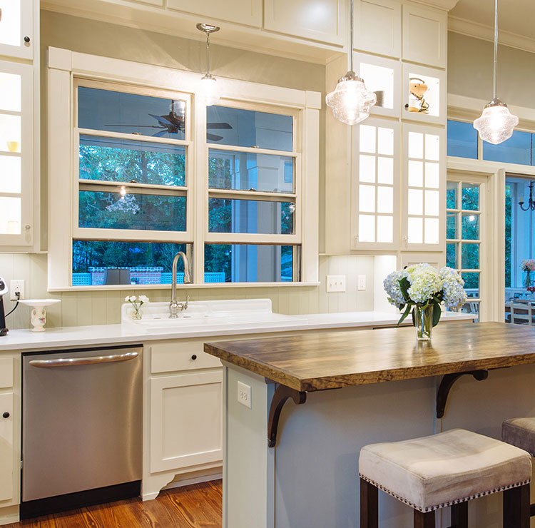Bright kitchen with white cabinets and crystal pendant lights, featuring large windows with garden view