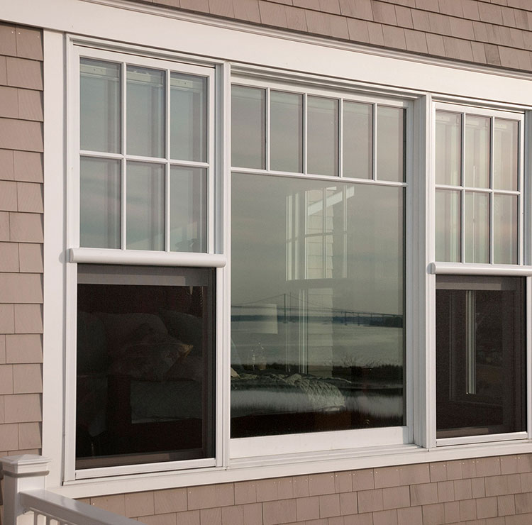 Triple-pane sliding window with white trim on beige exterior, showcasing coastal water view