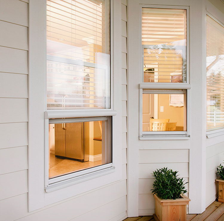 Modern white home exterior with retractable window screens, warm interior lighting, and decorative planter boxes on the porch