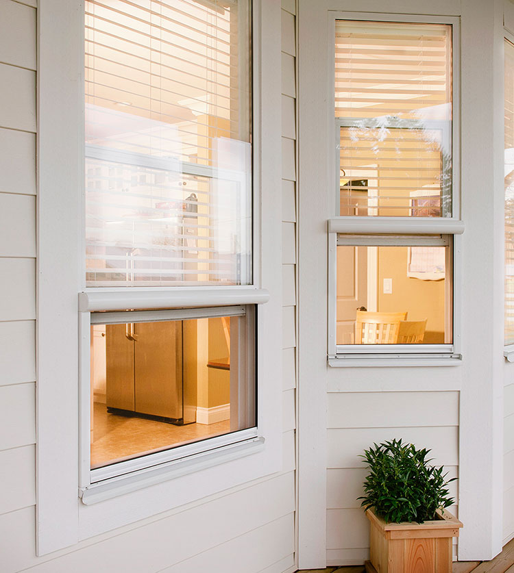 Modern white home exterior with retractable window screens, warm interior lighting, and decorative planter boxes on the porch